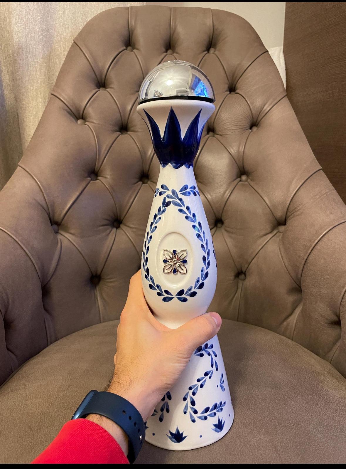 bottiglia Clase Azul Reposado in ceramica bianca e blu dipinta a mano con tappo argentato su sedia imbottita marrone