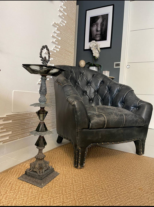 posacenere vintage italiano in metallo e vetro con supporto decorativo in legno stile mid century accanto a poltrona in pelle nera
