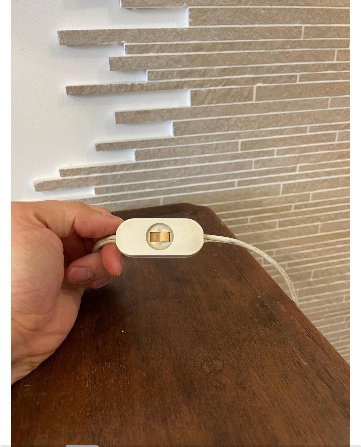 Lampada da tavolo elegante in ceramica bianca e dettagli in ottone con interruttore a cavo su tavolo in legno.