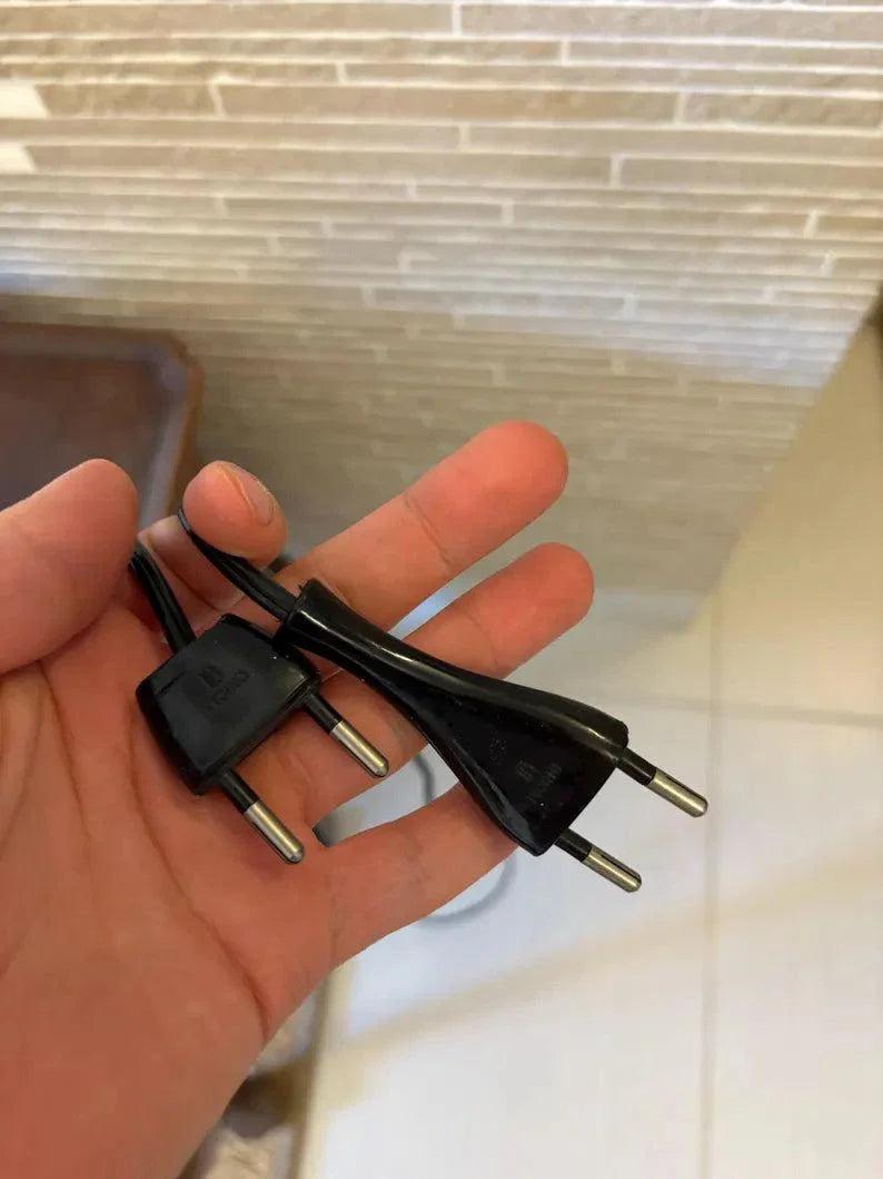 cavo con spina elettrica nera in mano su sfondo pavimento piastrellato e muro decorativo