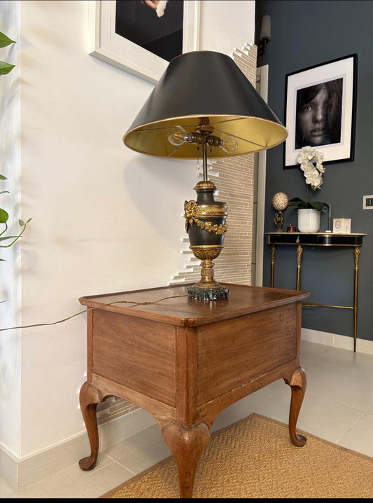 Lampada da tavolo stile Impero francese in metallo nero e ottone dorato con base in marmo, design vintage e decorazioni classiche su tavolino in legno.